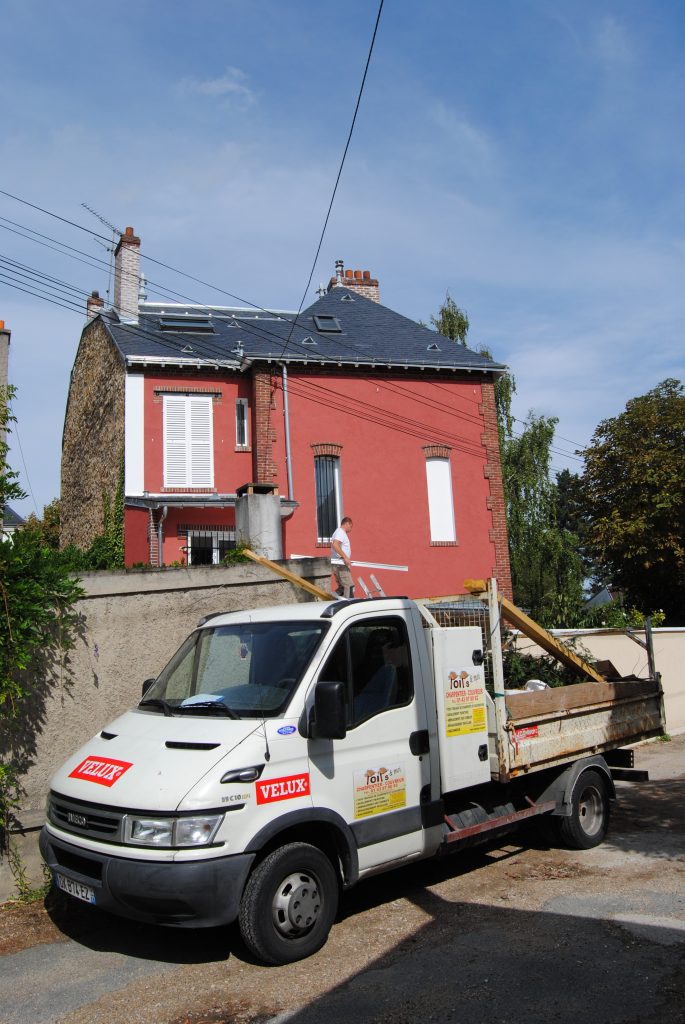 Maison rouge avec tuiles noir et camion de rénovation dans l'entrée